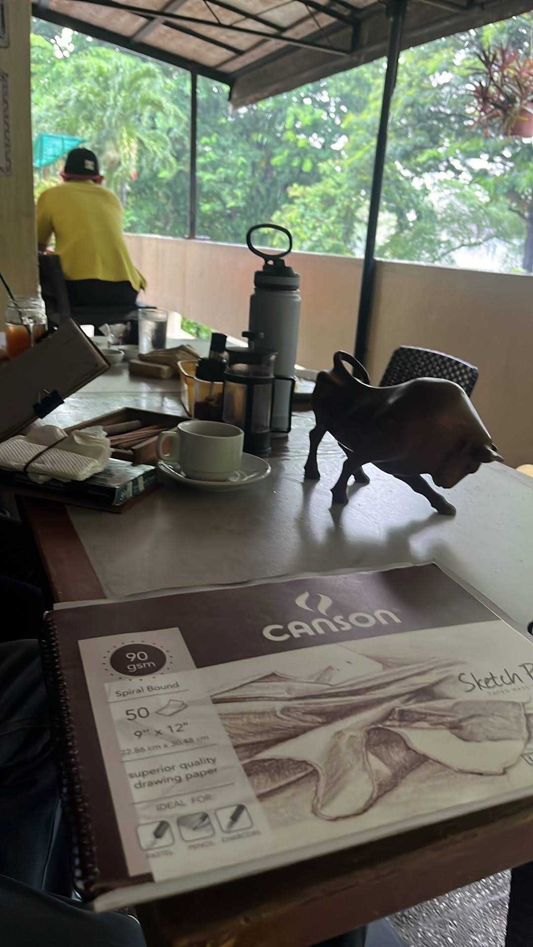 Sketch pad, coffee, and a bull sculpture on a cafe table